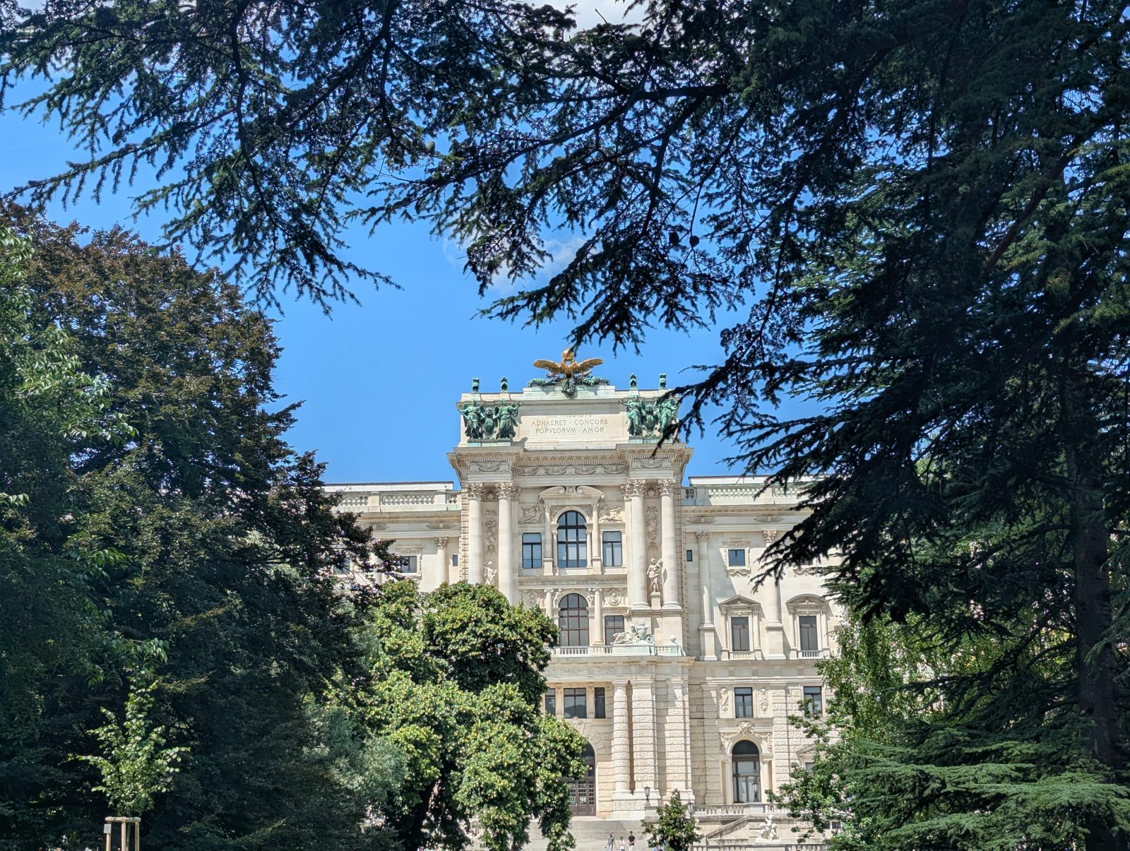 Elegant historic building in Vienna framed by tall trees, with a bright blue sky above.