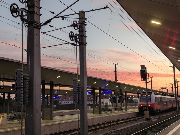 Photo of trainstation with two tracks during sunrise. One train standing in front of platform on the far right side.