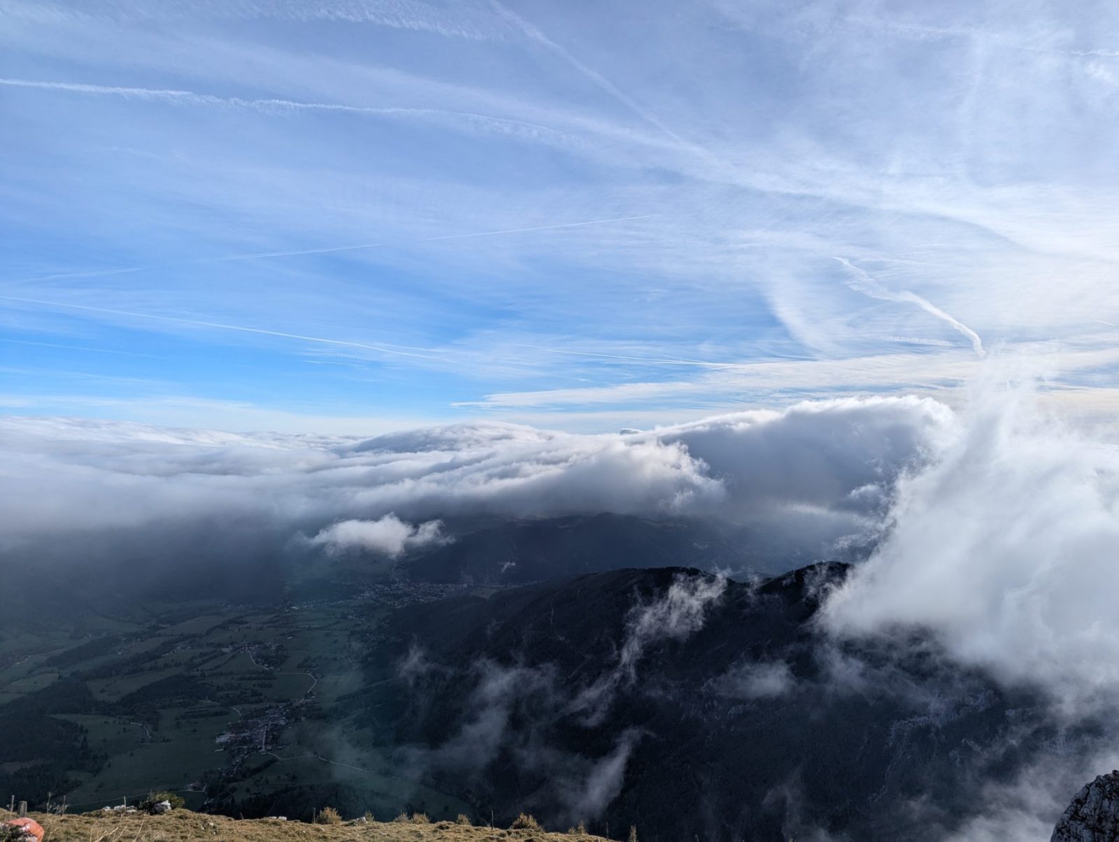 View from the Schneeberg summit in Lower Austria, showing a rocky outcrop above misty clouds and green valleys hidden below.