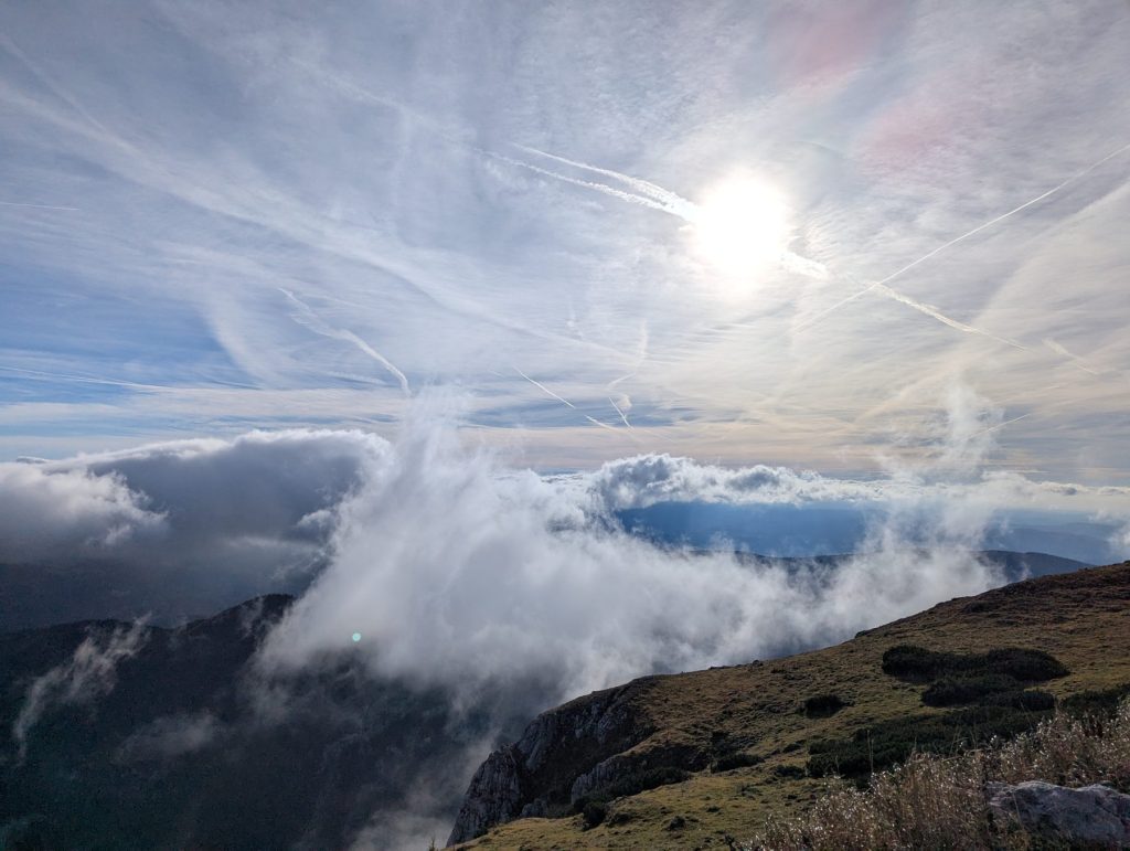 View of clouds being captured by a mountain. Sun is up high.